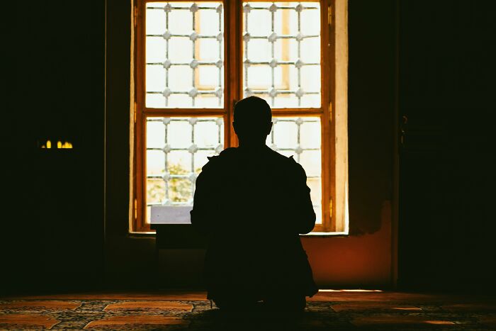 Silhouette of a person sitting alone in front of a window in a dimly lit room, creating a creepy and unsettling atmosphere.