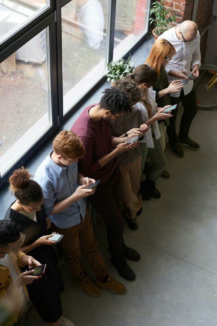 People standing in a line, absorbed in their phones, highlighting social norms to reevaluate.