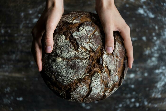 Hands holding a rustic round loaf of bread, resembling a fancy yet affordable home hack.