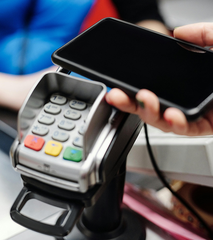 A person using a smartphone for contactless payment on a card reader.