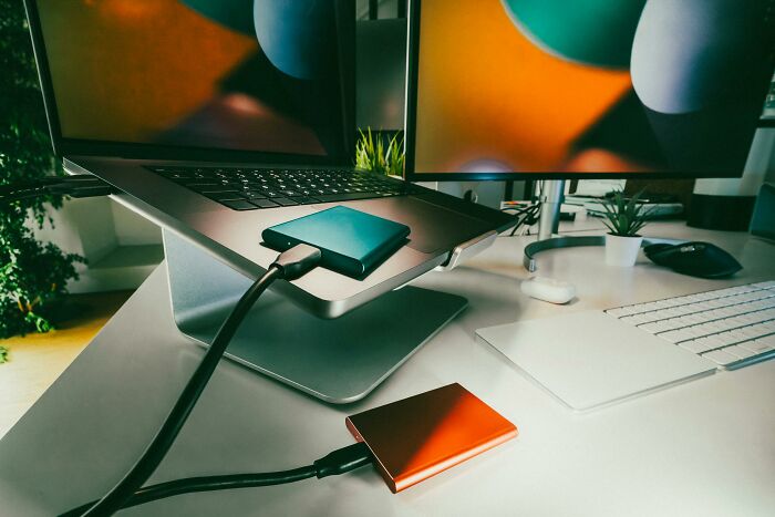 Laptop connected to colorful external hard drives on a desk with a keyboard and mouse nearby.