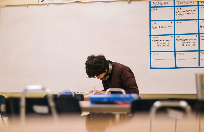 Student displaying genius, focused on writing in an empty classroom with a calendar on the whiteboard behind.