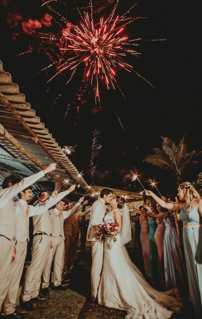 A wedding couple kisses under fireworks, surrounded by guests holding sparklers; a social norm often romanticized.