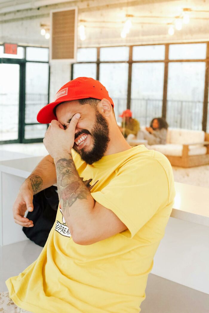 Man in a yellow shirt and red cap laughing, showcasing intriguing facts in a casual setting.