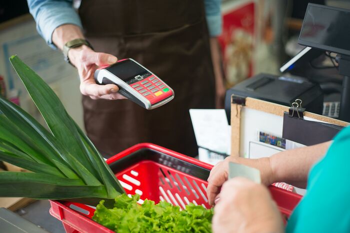 Person using a card reader to pay for groceries in 2025.