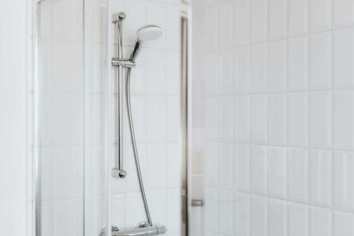 Modern showerhead in a spotless, white-tiled bathroom, highlighting a possibly creepy and unexplainable ambiance.