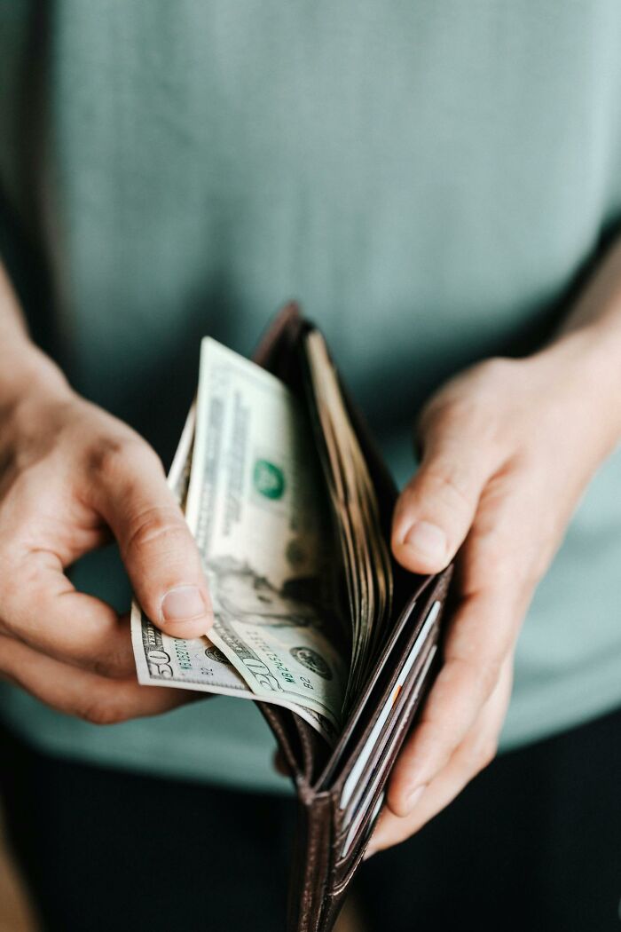 Hands holding a wallet with cash, highlighting intriguing facts about money handling.