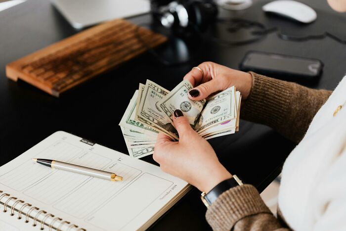 Person counting money at a desk, highlighting unaffordable costs for the middle class.