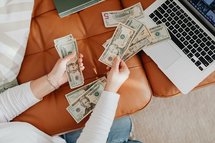 A person counting money next to a laptop, illustrating millennials' financial challenges in adulthood.