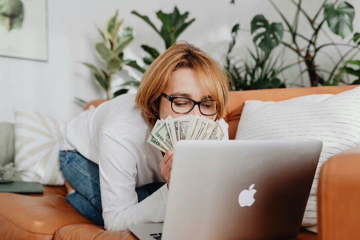 Person holding money in front of a laptop, symbolizing financial deceit or scams.