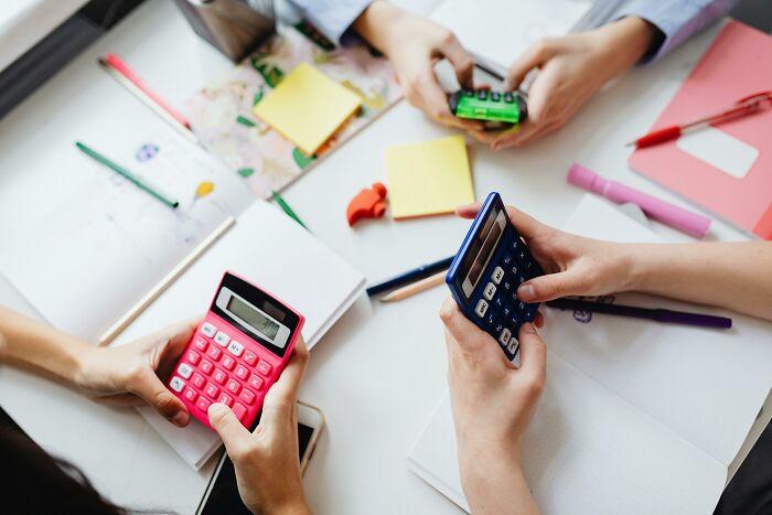 Hands using colorful calculators on a cluttered desk, showcasing human genius in problem-solving activities.