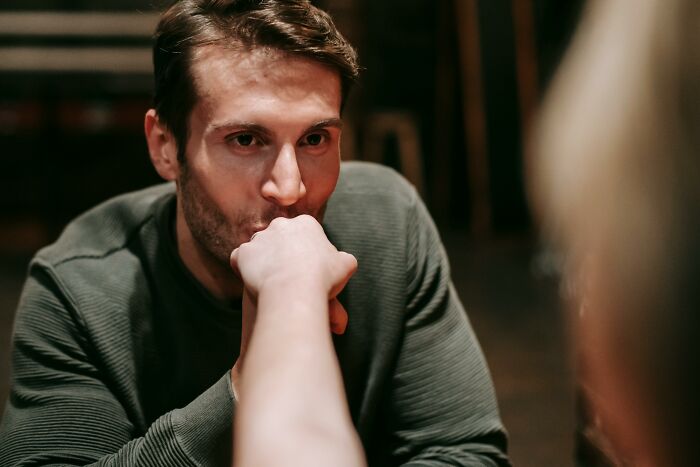 Man sitting at a table, biting someone's hand, depicting creepy and disturbing behavior in a dimly lit setting.