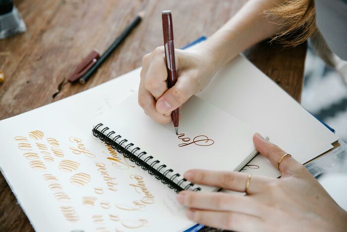 Person practicing calligraphy with pen and notebook, symbolizing millennial creativity in adulthood.