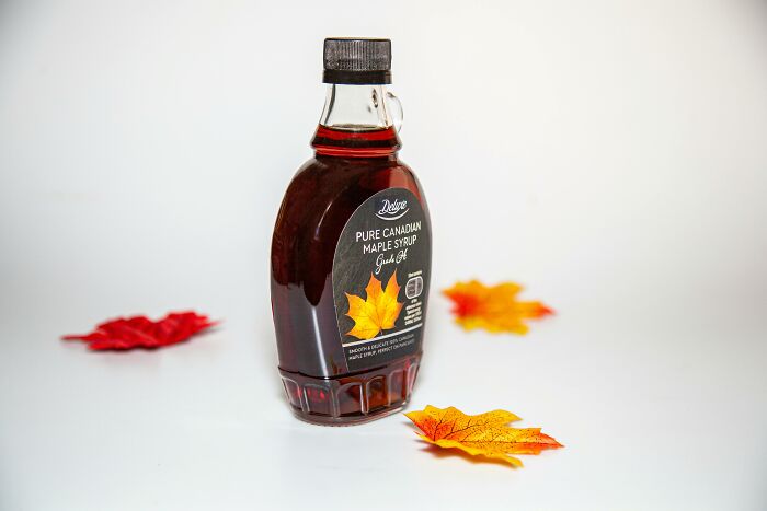 Bottle of Canadian maple syrup surrounded by colorful autumn leaves, highlighting new facts about syrup in the community.