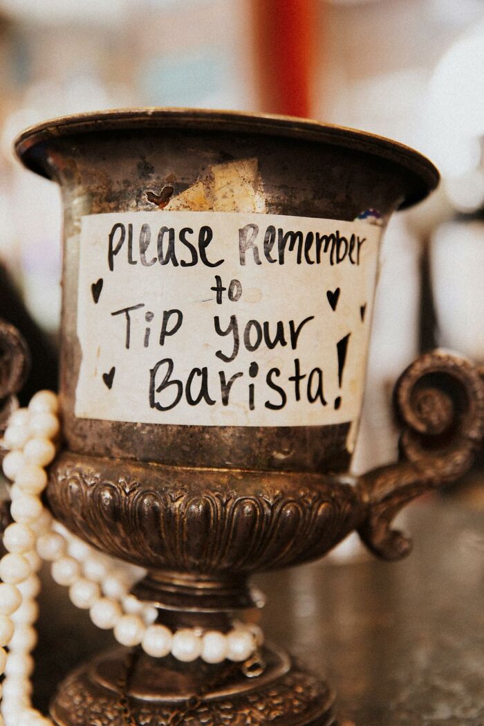 A tip jar with a note saying "Please remember to tip your barista," highlighting social norms.