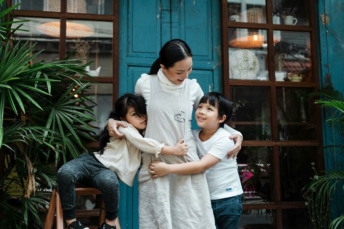 Woman hugging two kids, smiling and happy, in front of a blue door, capturing the feeling of being in a different country.