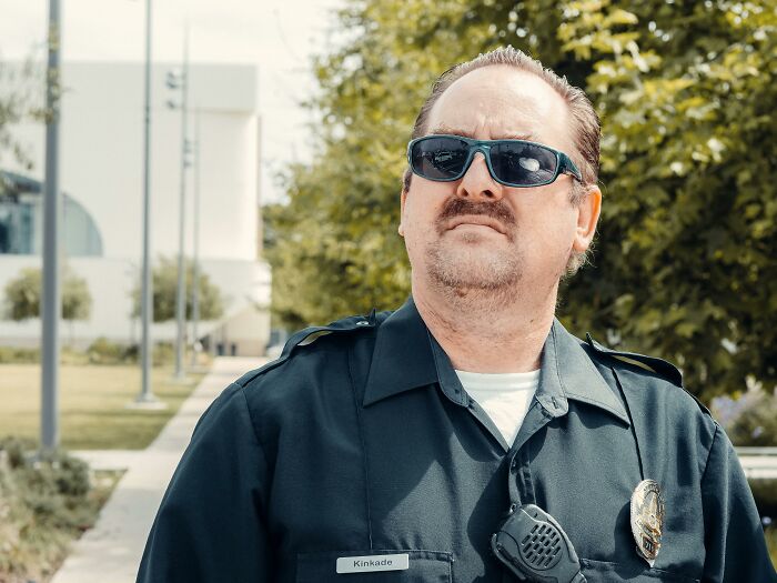 Police officer in uniform wearing sunglasses, standing outdoors.