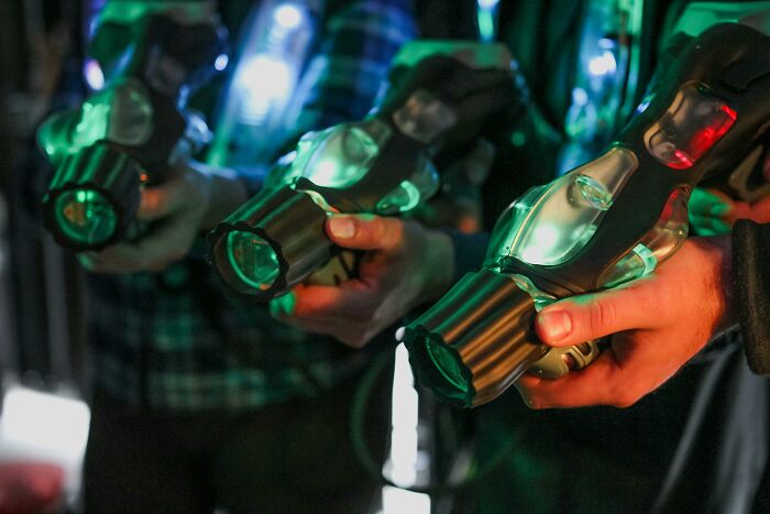 People holding laser tag guns, illuminated in a dim setting, creating a creepy and unexplainable atmosphere.