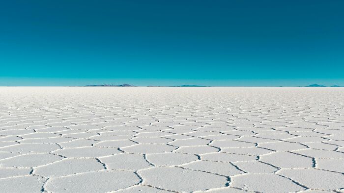 Expansive salt flats under a clear blue sky, resembling a unique cracked pattern in Tuscany, Italy.