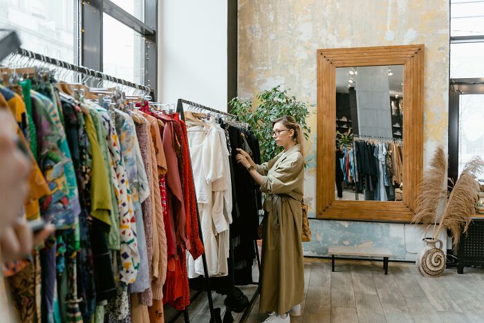 Person browsing clothes in a vintage store with a large mirror and plant in the background.