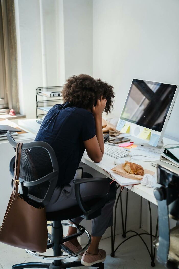 Person overwhelmed at work, sitting at desk with computer and a croissant, reflecting social norms that should change.