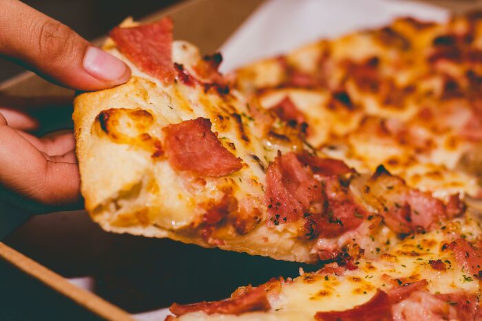 Close-up of a hand grabbing a slice of pepperoni pizza.