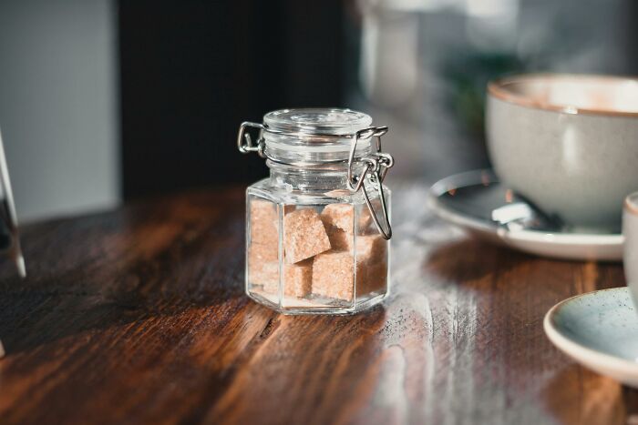 Glass jar with sugar cubes on a wooden table.