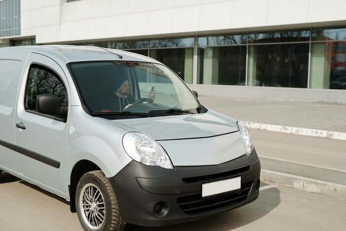 Person in a gray van parked on a city street, looking at a phone, possibly depicting a revengeful job exit.