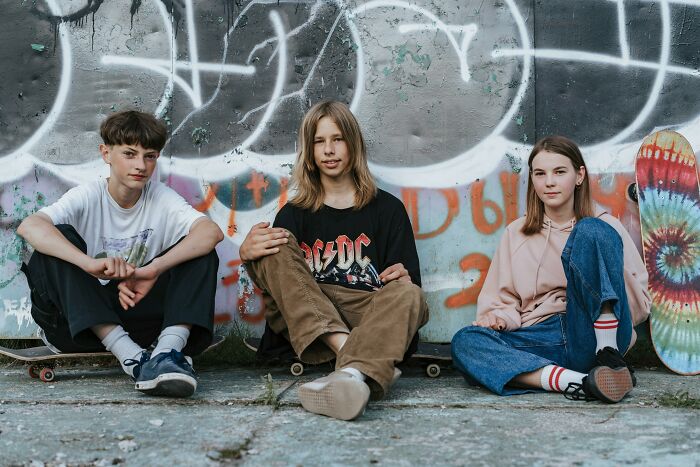 Three teenagers sitting on skateboards in front of a graffiti-covered wall, representing carefree youth.