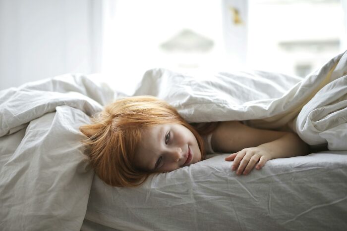 A child lying in bed wrapped in white sheets, illustrating the comfort of expensive items.