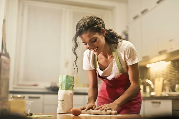 Woman baking in a kitchen, smiling while kneading dough.