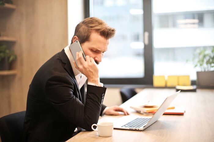 Man in suit using a smartphone and laptop at a desk, illustrating non-sexual things men do that turn women on.