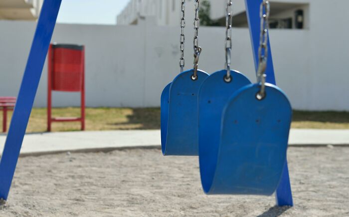 Empty blue swings in a playground, evoking unsettling and creepy feelings.