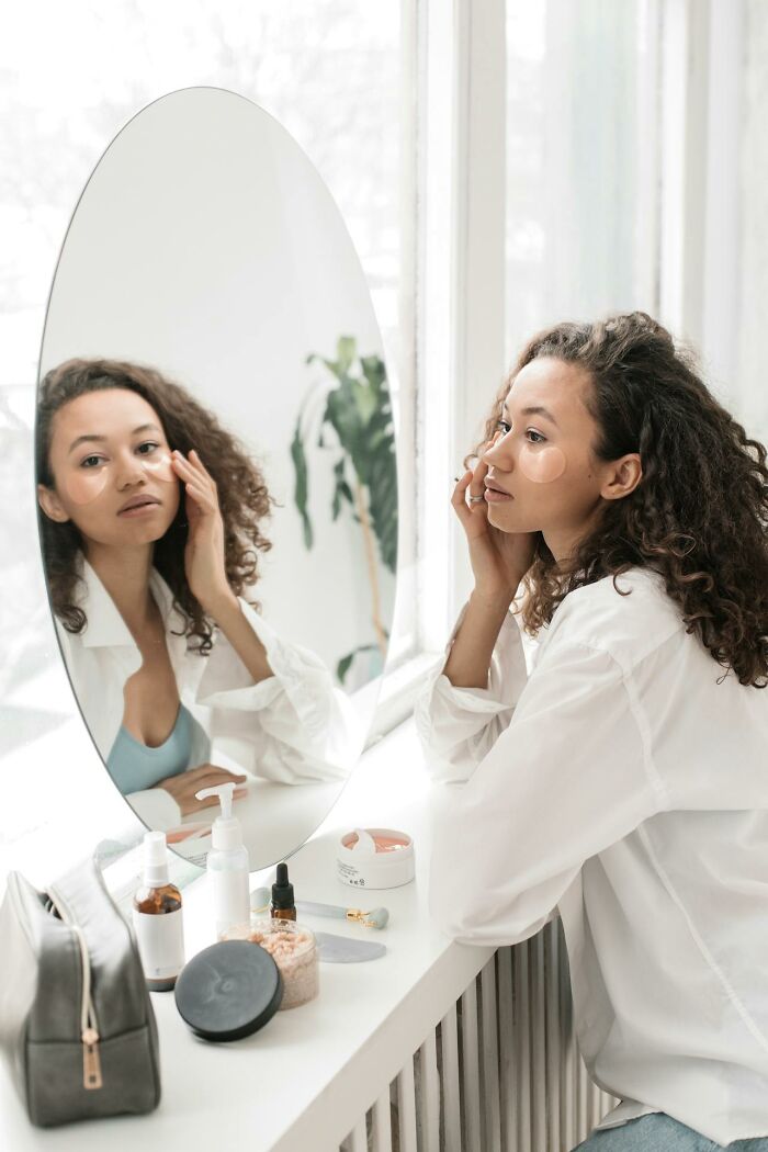 Woman applying skincare before mirror, challenging social norms.