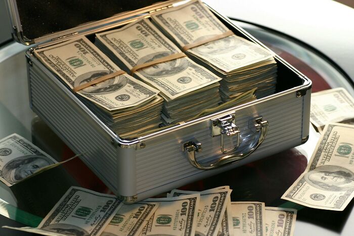 Open metal briefcase filled with stacks of hundred-dollar bills, illustrating a concept related to the biggest scam.