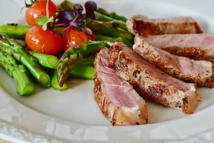 Grilled meat and asparagus with tomatoes on a white plate, illustrating food becoming unaffordable for the middle class.