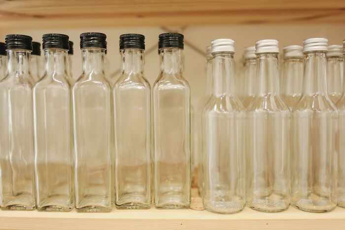 Empty glass bottles on wooden shelves, aligned and staggered, some with black caps and others with white caps.