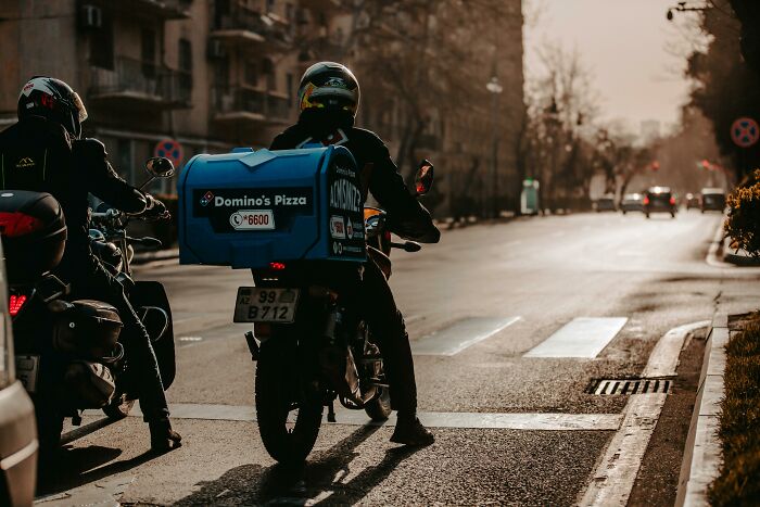 Delivery driver on a motorcycle with a pizza box in the city, representing awkward delivery stories.