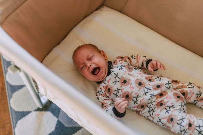 A crying baby in a crib, wearing a floral outfit.