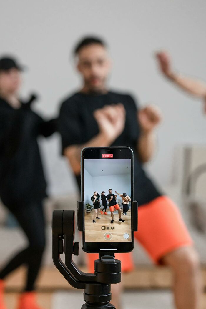 Smartphone on tripod filming people dancing; highlights social norms during a fun activity.