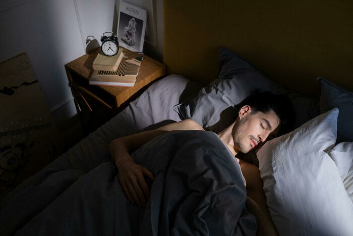 A man sleeping peacefully in bed, with a dimly lit room and an alarm clock on the bedside table.