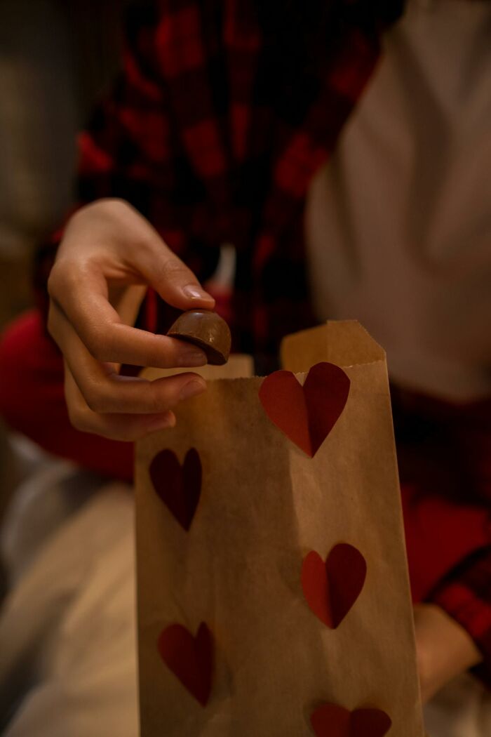 A person in a plaid shirt placing a chocolate in a gift bag with heart designs, illustrating non-sexual things that turn women on.