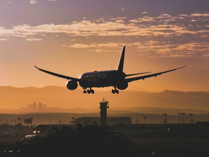 Airplane landing at sunset, showcasing human engineering genius against a dramatic sky backdrop.