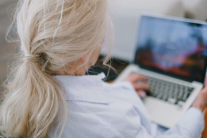 Woman with grey hair using a laptop, viewed from behind, creating a mysterious or creepy atmosphere.