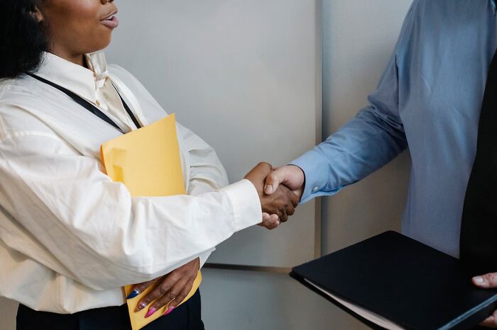 Two people shaking hands, one holding a yellow folder, symbolizing outdated social norms.