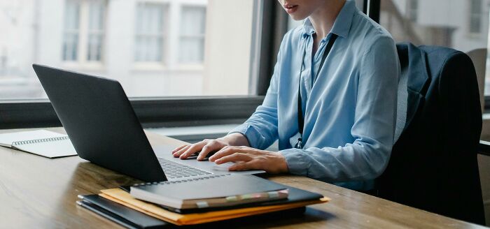 Person in blue shirt using a laptop at a desk, illustrating a potential unethical life hack in a work setting.