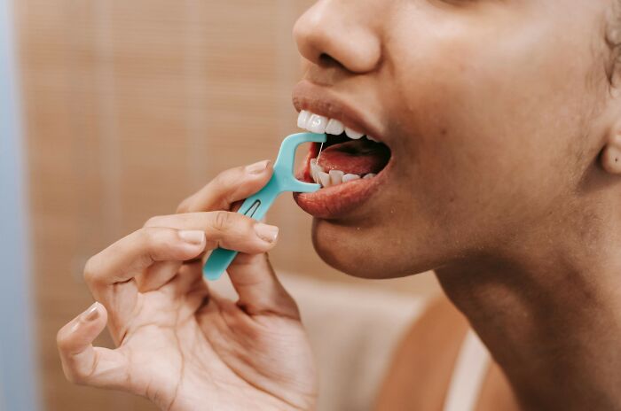 Person using a teal floss pick for dental care, highlighting one of the expensive items worth spending money on.