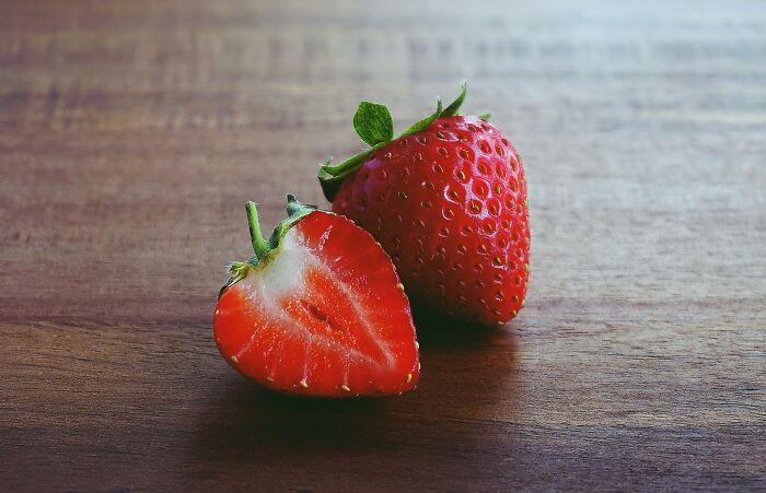 Whole and half strawberry on wooden surface showcasing weird nature quirks.