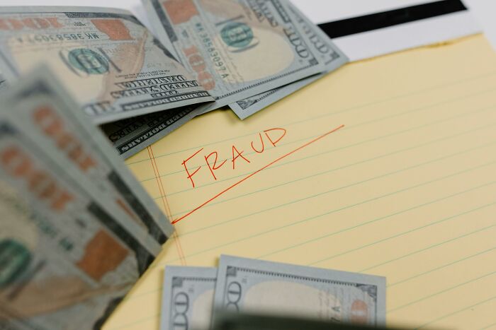 Yellow notepad with "fraud" written, surrounded by hundred-dollar bills, highlighting resume red flags and concerns.