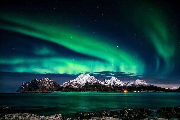 Northern lights over snowy mountains and sea.